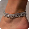 Silver gold plated minimalist Cuban link anklets worn around the ankle of a person.