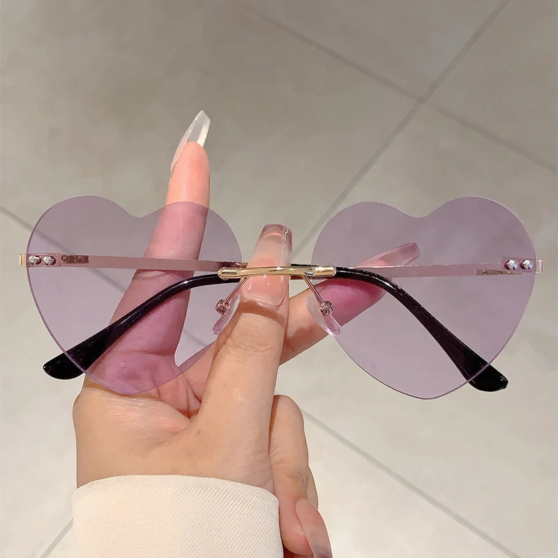 Eine Hand hält eine Vintage-Sonnenbrille in herzförmiger Form mit violetten Gläsern und goldenen Akzenten.