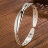 A close-up shot of a silver bell bangle bracelet with a textured finish resting on a wooden surface.