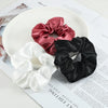 Three satin scrunchies in shades of pink, black, and white are displayed on a white plate.