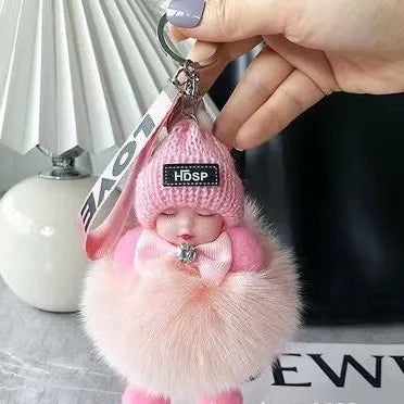 A pink fluffy cartoon plush doll keychain is being held by a hand against a dark background.