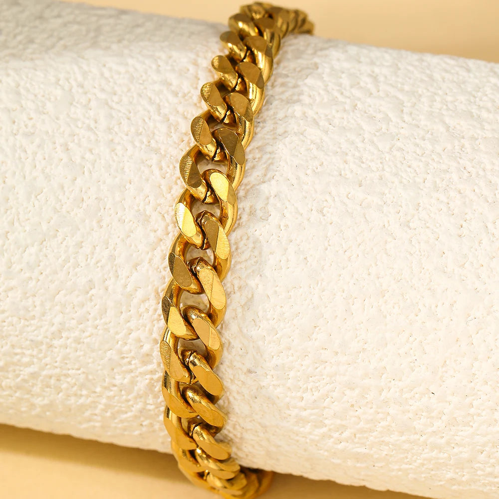 A gold-colored multi-chain stainless steel anklet is shown resting on a white fabric background.
