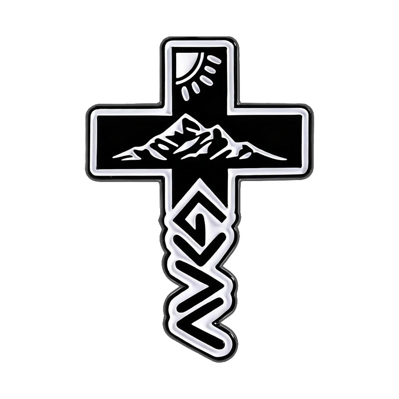 Broche émail noire en forme de croix avec un motif de montagne et de rayons de soleil.