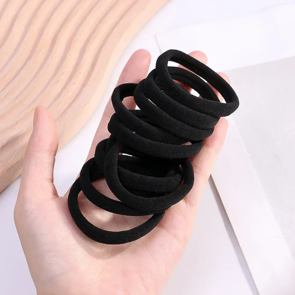 A hand holds a stack of black elastic hair bands for ponytail and hair ties.