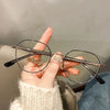 Une main tient une paire de lunettes vintage classiques anti-lumière bleue sur un fond clair.