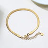 A gold-toned stainless steel snake chain anklet laid out on a white surface.