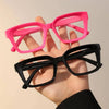 A hand holds a pair of pink and black square reading glasses against a light background.