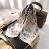 A luxury silk scarf in white and floral patterns is draped over a dark box on a light surface.