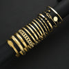 A stack of gold geometric minimalist bracelets on a black cylindrical display rod.