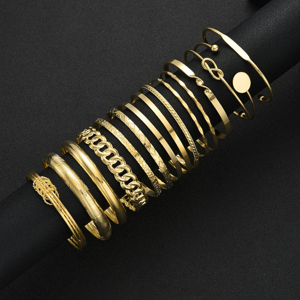 A stack of gold geometric minimalist bracelets on a black cylindrical display rod.