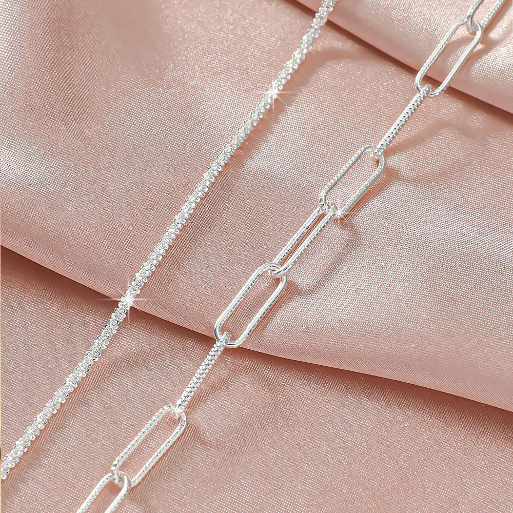 Silver plated CZ anklets draped against a soft pink fabric background