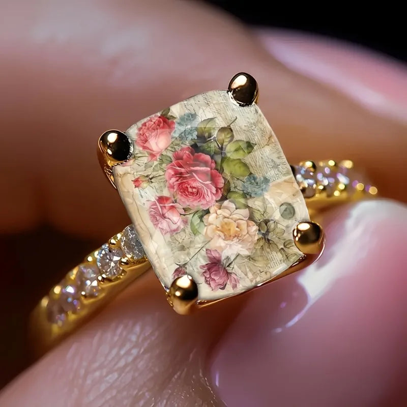 Bague statement dorée avec illustration florale rose carrée et accents dorés.