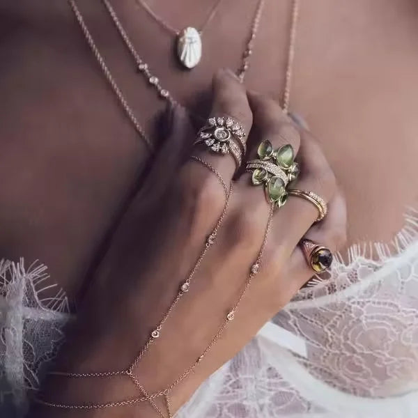Une main portant un bracelet délicat en or avec un charm à cadre géométrique et un collier pendentif en argent.