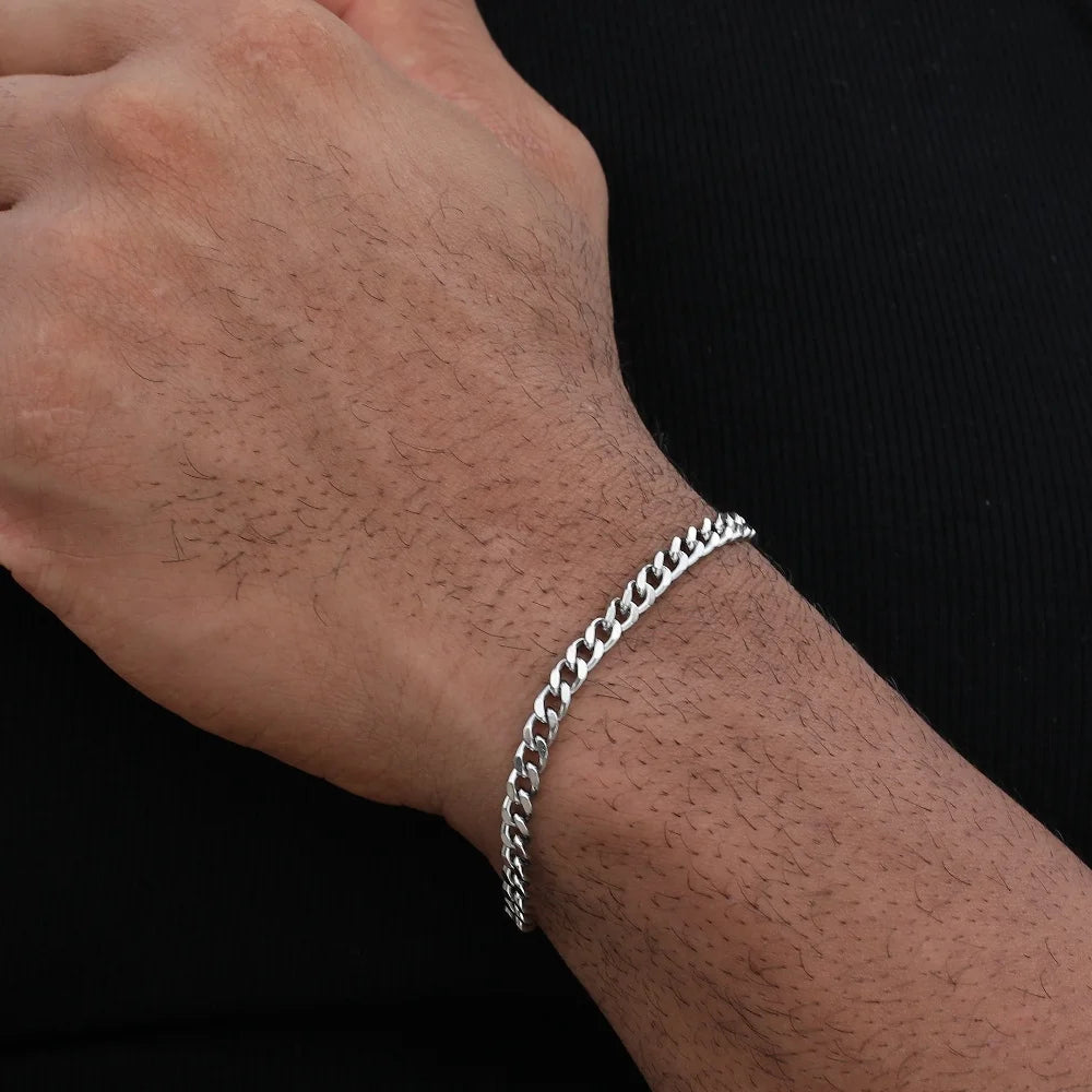 A close-up of a man's wrist wearing a silver stainless steel Cuban link bracelet.