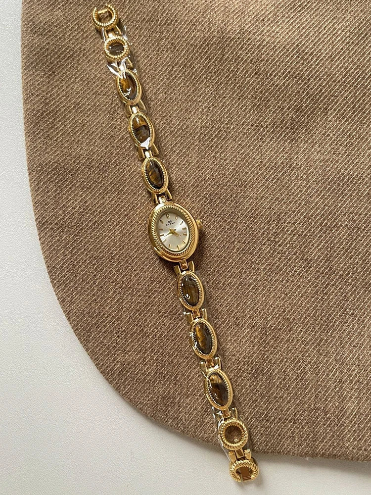 Montre-bracelet en quartz ton or avec cadran ovale et bracelet maillons sur fond de tissu marron.