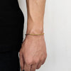 A close-up of a hand wearing a gold stainless steel twisted chain bracelet on the wrist.