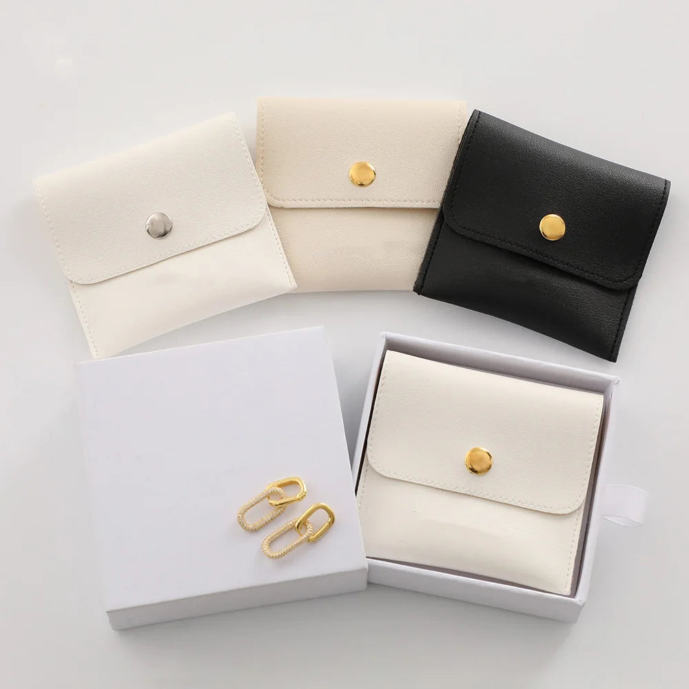 A set of elegant cream and black PU leather jewelry pouches with gold snap buttons displayed on a white surface.