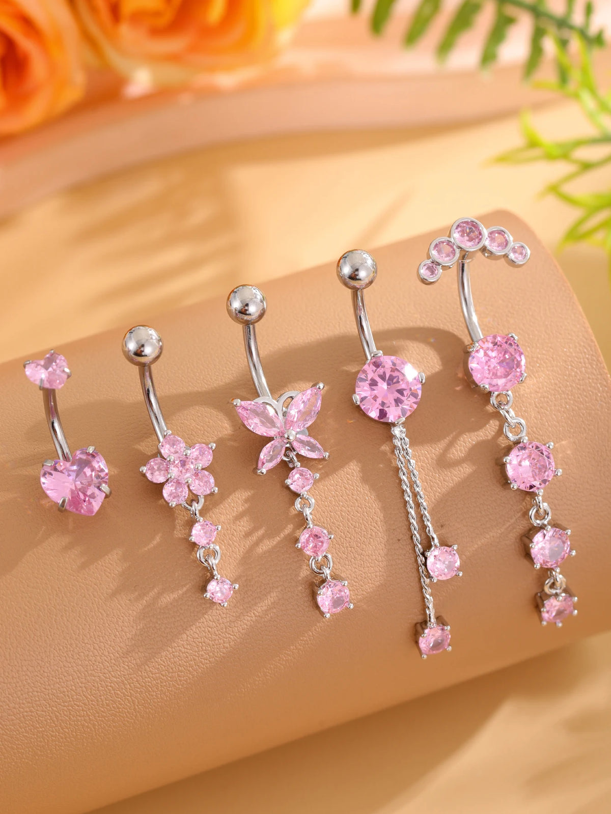 A set of five gold stainless steel dangled belly button rings featuring pink and clear gemstone accents.