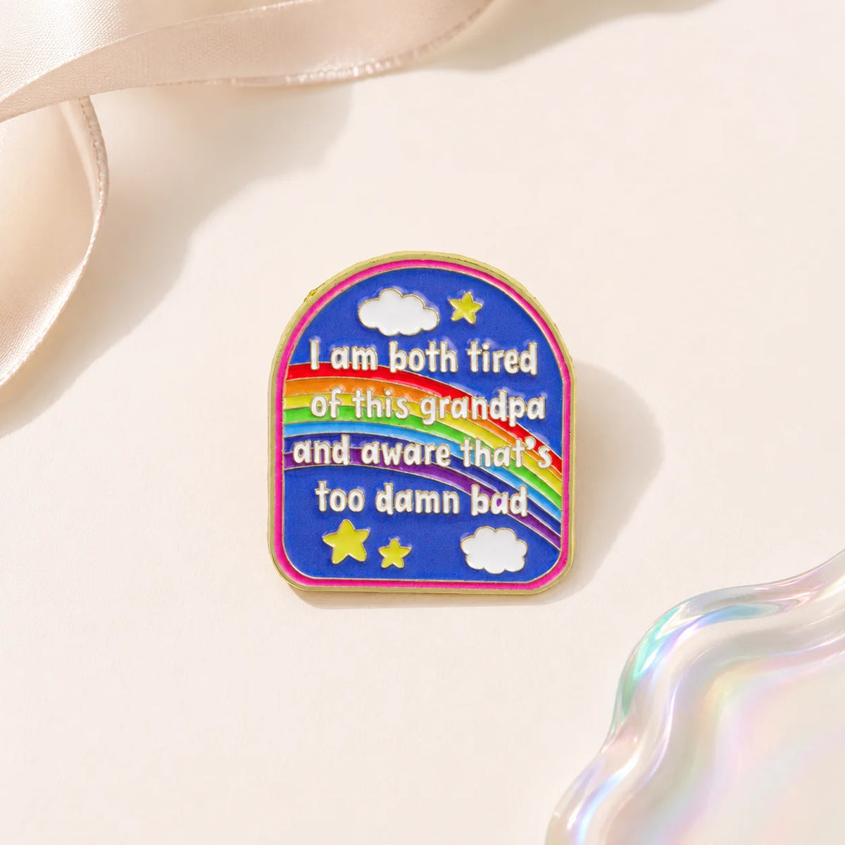 A colorful enamel pin featuring clouds and stars with the text I am both tired of this grandpa and aware that's too damn bad