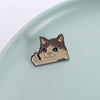 A small enamel pin depicting a cute cat face with closed eyes and a happy expression.