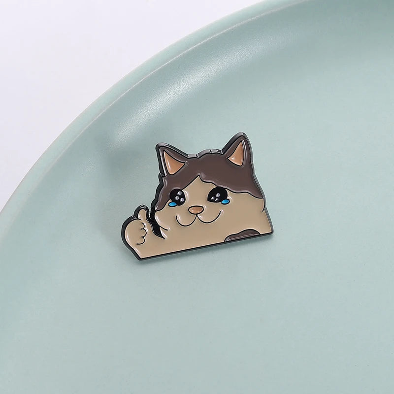 A small enamel pin depicting a cute cat face with closed eyes and a happy expression.