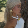 A woman wearing a beige bohemian lace trim shawl draped over her head, posing outdoors against a tree.