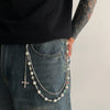 A close-up of a luxury pearl cross pendant necklace draped over the pocket of blue jeans.