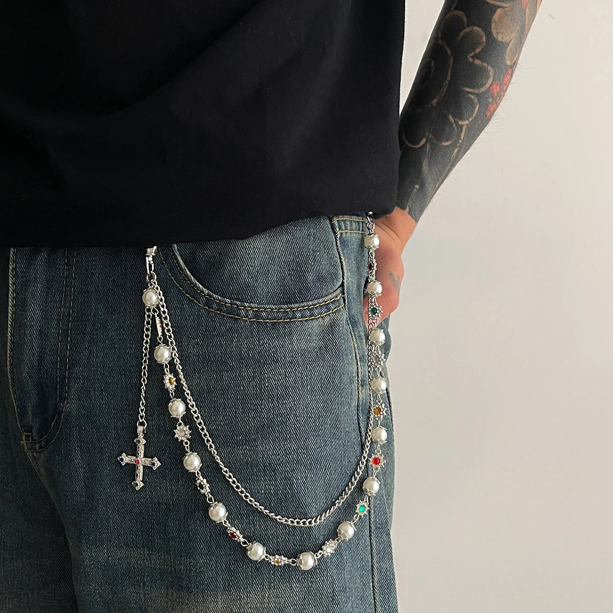 A close-up of a luxury pearl cross pendant necklace draped over the pocket of blue jeans.