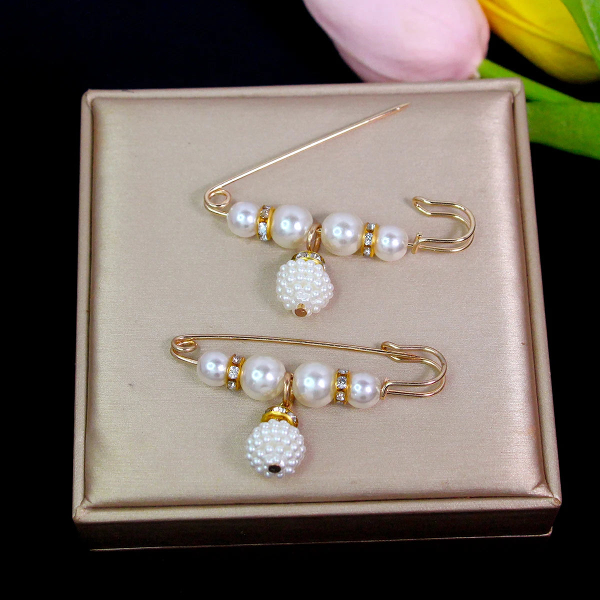 A delicate gold-toned adjustable pearl brooch featuring multiple strands of white pearls displayed in a rectangular box.