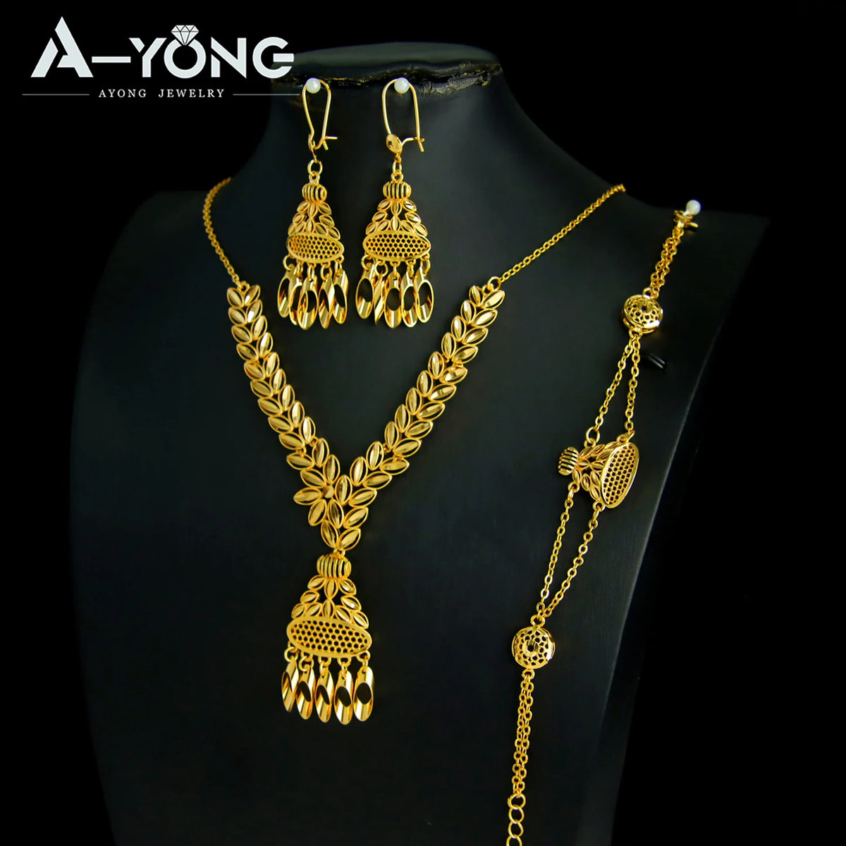 A set of luxury gold plated bridal jewelry featuring ornate earrings and a layered necklace displayed on a black mannequin.