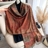 A richly patterned bohemian paisley shawl in shades of rust and olive green draped over a light-colored armchair.