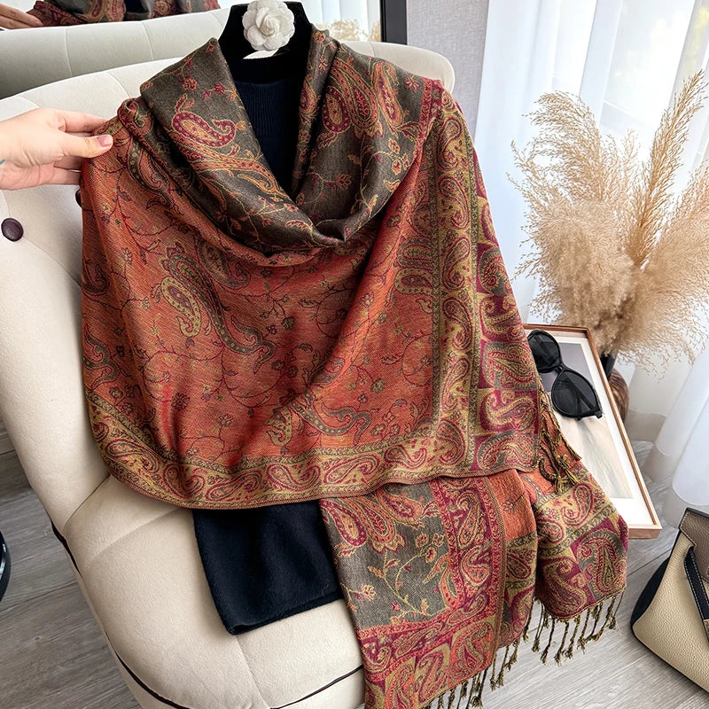 A richly patterned bohemian paisley shawl in shades of rust and olive green draped over a light-colored armchair.
