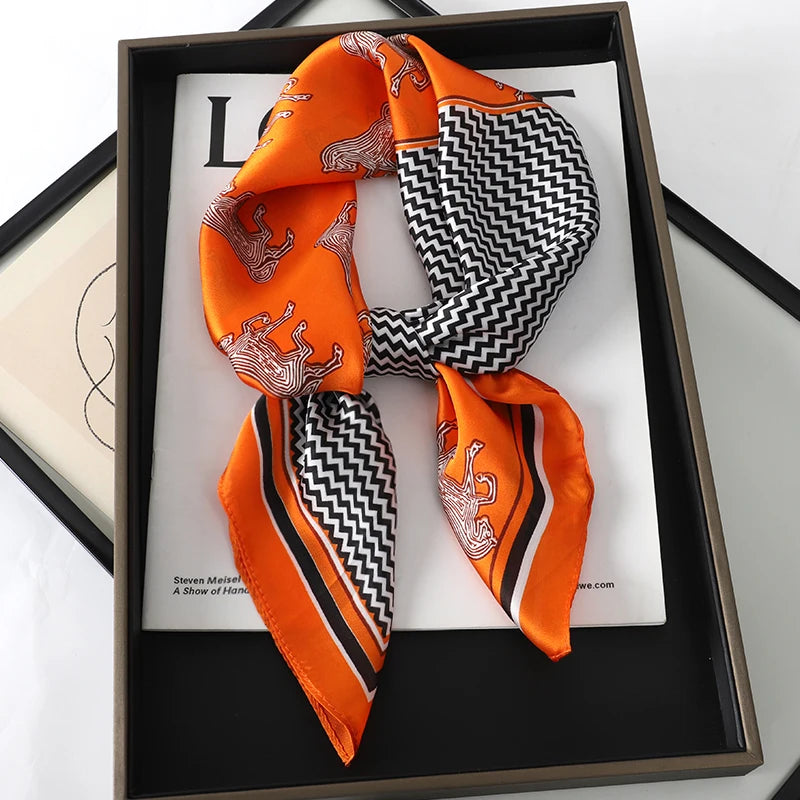 An orange silk scarf featuring a black geometric pattern and an embroidered design, displayed in a dark frame.