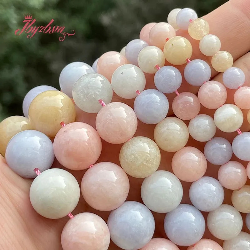 A hand holds a collection of smooth, round jade-colored beads in various shades of pink, white, and light blue.