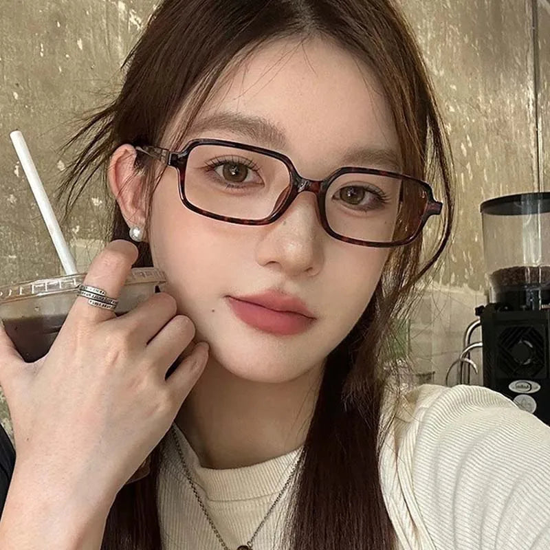 صورة مقربة لامرأة ترتدي نظارات شمسية مربعة كلاسيكية وهي تحمل مشروباً.