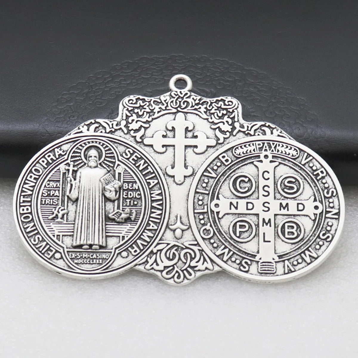 Silver Saint Benedict protection medal with a cross and inscription on a dark background