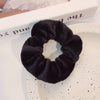 Un élastique pour cheveux en tricot flou noir est exposé sur une assiette blanche à côté d'un livre.