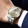 A close-up of a stainless steel quartz watch worn on a wrist, featuring a gold-toned dial and bracelet.