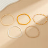 A collection of five beaded bracelets and anklets in various shades of yellow, white, and orange laid on a beige surface.