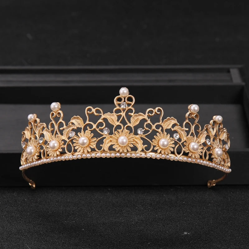Gold rhinestone bridal tiara headpiece with pearl accents displayed on a black surface.