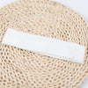 A white knitted elastic headband lying on a natural woven mat.