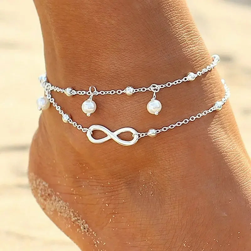 Boho silver plated friendship anklet worn on a woman's foot against a sandy background