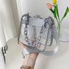 Bolso cruz de PVC plateado y transparente con detalles de cadena sostenido en la mano de una persona.