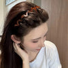 A woman with long dark hair wears a brown resin wave toothed headband styled in an updo.