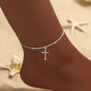 A delicate sparkling zircon heart cross anklet worn on a person's ankle.