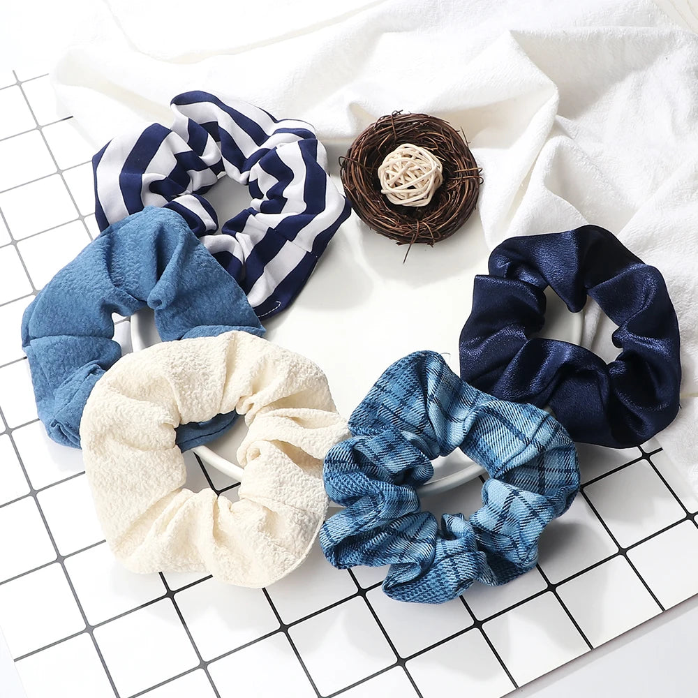 A pack of three colorful knitted hair scrunchie headbands in blue, white, and navy are displayed on a white surface.