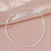 A delicate sparkling zircon heart cross anklet laid on a soft pink satin fabric.