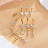 A set of gold dangle curved belly piercing jewelry featuring heart and flower designs with pearl and diamond accents.