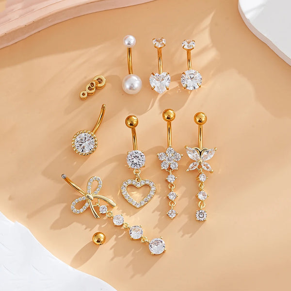A set of gold dangle curved belly piercing jewelry featuring heart and flower designs with pearl and diamond accents.