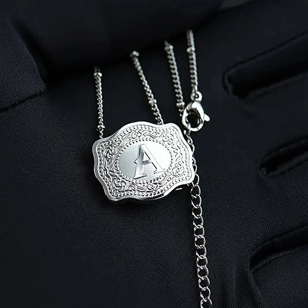 Silver initial letter pendant necklace with a detailed filigree design hanging from a chain.